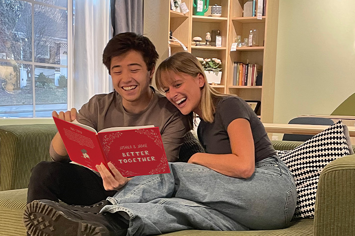 Boyfriend and girlfriend read the customized Book of Us that has their names and "Better Together" on the red cover.